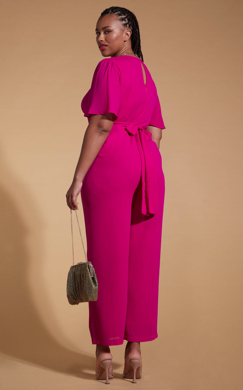 Model faces backwards wearing a pink dancing leopard jumpsuit with a gold clutch bag.