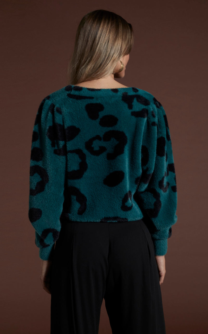 Dancing leopard model standing with back to the camera wearing bambino cardigan in black on forest green leopard with black trousers