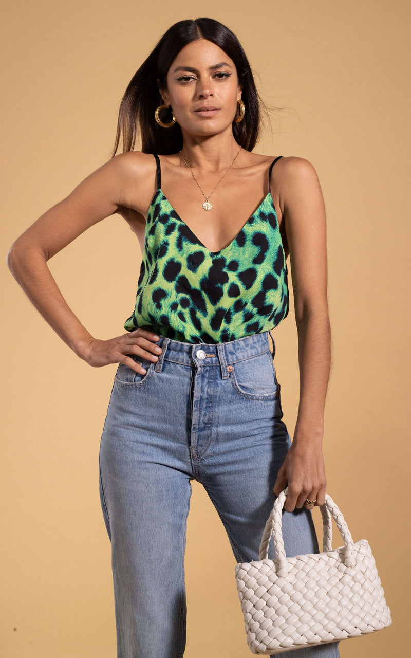 Dancing Leopard model standing with hand on hip wearing Birdie cami top in lime leopard holding woven bag and wearing light wash blue jeans