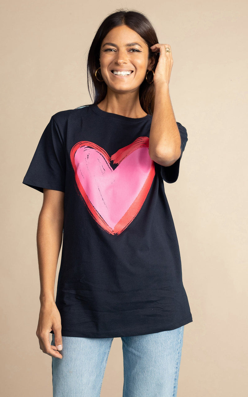 Dancing Leopard model standing forwards with right hand In hair wearing navy blue heart charity t-shirt for Choose Love untucked over  light wash denim jeans