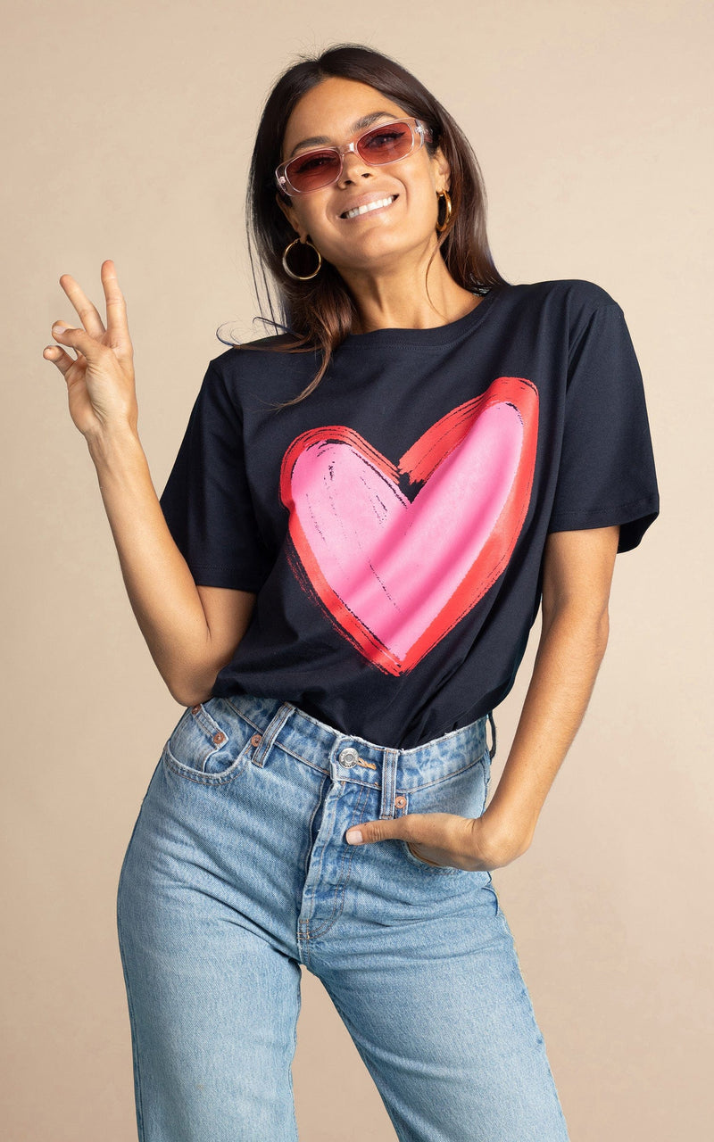 Dancing Leopard model standing forwards with left hand In raised peace sign wearing navy blue heart charity t-shirt for Choose Love tucked into light wash denim jeans